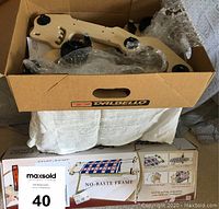 Partial assembled wooden quilt frame components packed in a cardboard box with bubble wrap and assembly instructions visible.