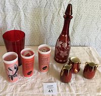 Full lot view showing red glass decanter, 3 Seattle World's Fair themed tumblers, 3 small lusterware vases, and 1 plain red glass vase on a beige cloth
