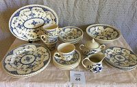 Blue and white ironstone china set displayed on fabric surface, showing the various plates, cups, serving bowl, and platter in matching floral pattern.