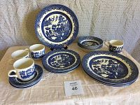 Photo showing full set including plates, bowls, cups, and saucers with Blue Willow pattern on a beige tablecloth.