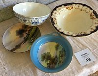 Four ceramic pieces on beige cloth: one blue and white floral vintage bowl, one vintage plate with floral and scalloped edges, and two additional bowls with painted landscape scenes, one with blue rim and one neutral rim.