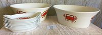 Two large white ceramic bowls alongside ten white appetizer plates, all decorated with red crab motifs.