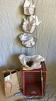 Full view of the red plastic milk crate with items inside, the wire hanging basket with three baskets hung vertically, and metal stakes leaning against the wall.