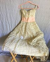 Full length view of vintage off-white lace strapless dress with pink taffeta waistband, displayed hanging against a gray backdrop.