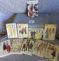 Photo of the collection of 10 vintage sewing pattern envelopes from the 1970s arranged on a couch, showing cover illustrations for women's, children's clothing and hats.
