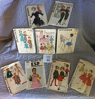 Full lot of 10 vintage 1960s women and girls sewing patterns shown in a pile on blue fabric background.