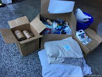 Overview of all painting supplies including boxes, tarps, brushes, rollers, and various containers on concrete floor