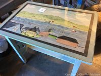 Top view showing the hand painted village and water scene on table surface under glass