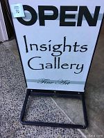 Front view of metal fold-up sidewalk sign with 'OPEN Insights Gallery Fine Art' lettering in black vinyl on white panel, showing the weighted base and foldable frame.