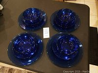 Top-down view of four sets of blue glass dishes arranged on table, each including a dinner plate, salad plate, and bowl.