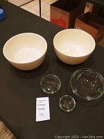 Six kitchen bowls displayed together on table, including two large white bowls and three smaller clear glass bowls.