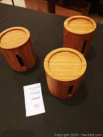 Three bamboo canisters arranged in a group on a dark surface, showing natural wood grain and wooden lids.