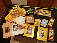 Overview of collection on black table showing wine cork board shaped as coffee cup, framed prints, and placemats.