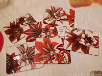Photo shows set of 3 rectangular hard-backed placemats and 3 square coasters. Each item has a red and white floral hibiscus-like pattern with leaf accents.