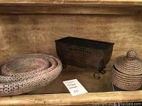 Three nested woven baskets, rectangular metal basket with scroll feet, and a lidded woven basket arranged on a shelf.