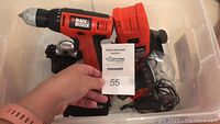 Photo showing the cordless drill and handheld screw gun with battery and charger, with a lot number card held in view.