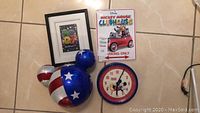 Photo of large Mickey ears ornament painted with red, white, and blue stars and stripes, round Mickey Mouse clock, Mickey Mouse Clubhouse parking sign, and framed Disney artwork.