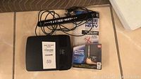 Photo showing a black TV Free Way digital antenna with cable, black Cisco Linksys E1500 modem/router, and TV Free Way packaging and user manual.