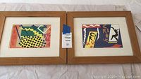 Photo showing two framed posters side by side with wood frames and white mats, designs in Fauvist style with bright colors and circus theme text.