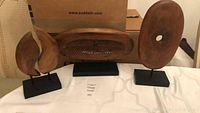 Three mid-century style wooden abstract sculptures on black base stands arranged side by side, showcasing shapes and carved details