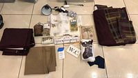Overview photo showing all items laid out together on tiled floor including curtain panels in tan, purple, plaid, brown bed skirt, key hanger, picture, basket, light bulb, knobs, rings, and clip light.
