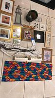 Top-down photo showing a variety of framed wall art, decorative items, rope curtain, window curtain with fish pattern and small shelves spread on floor.