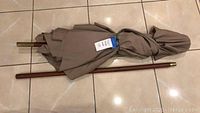 Tan outdoor patio umbrella folded closed with tan fabric canopy and wooden pole, placed on tiled floor.