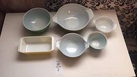 Full view of 5 vintage Pyrex bowls of various sizes and a yellow loaf pan on table.
