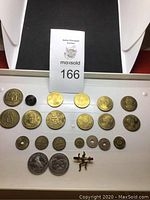 Full view of the collection displayed on white padding showing multiple gold-tone and silver-tone tokens and a small figure pin.