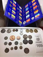 Coins displayed on a white tray beneath a blue folder with multiple country flags and coin denominations