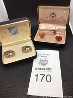 Photo of two sets of cufflinks in their original boxes with auction tag; one set with a dog motif and one pink set with tie pin.