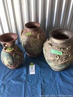 Group photo showing three pottery vases of varying sizes with textured leaf designs, arranged on a blue cloth.