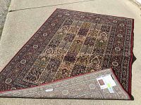 Area rug laid out on concrete showing full design with intricate pattern and red border, corner lifted to show backside with Ikea label.