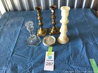 Front view of four candle holders including brass, glass, and alabaster along with a round coaster marked 'Nova Scotia'. Items placed on blue fabric.