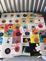 Top view of 31 vinyl 45 RPM records in various original sleeves arranged flat showing label logos and colors.
