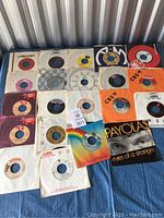 21 assorted 45 RPM vinyl records laid out on floor with various labels and sleeves visible