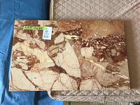 Close-up photo of a polished marble slab with beige, brown, and cream natural stone fragments.