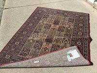 Image of the full Ikea area rug laid flat on a concrete floor showing the multicolor traditional pattern and corner flipped to reveal the underside tag.