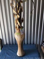 Full view of tall brown and beige glass vase with dried floral décor in a storage setting