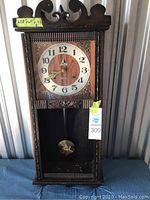 Full view of vintage Lava wooden wall clock showing overall condition including missing bottom glass panel and visible pendulum.
