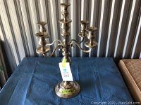 Front-angle photo of the silver plated five-arm candelabra placed on a blue cloth surface in front of a corrugated metal background.