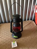 Full front view of black metal Beacon railway lantern with red glass globe and wire handle, showing overall condition and size.