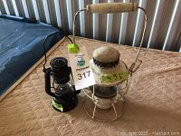 View of two lanterns side by side on a quilted brown surface: smaller black lantern labeled 7 inches and a larger white lantern labeled 9.5 inches.