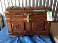 Front view of the wooden chest showing carved panels, brass corner accents, lock, and brass inlaid designs.