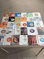Photo of 30 assorted 45 RPM vinyl records with labels from CBS, Mercury, WEA, Polygram and more. Various 80s popular music artists visible.