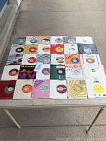 Photo showing 30 assorted 45 RPM vinyl records with original sleeves on a table, assorted record labels including PolyGram, CBS, and others.