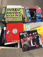 Photo showing a pile of colorful vinyl records with album covers including Herbie Hancock Mega-Mix and others.