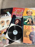 Photo showing several vintage vinyl record album covers and one vinyl record outside its sleeve, arranged on a surface.