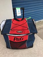 Front view of a large P&G cooler bag in red and navy blue with wheels and retractable handle.