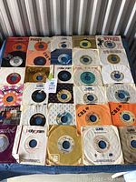 Photo showing a collection of 7-inch vinyl records with various brands such as RCA, CBS, Polydor, WEA, Polygram, and Columbia in original and generic sleeves.